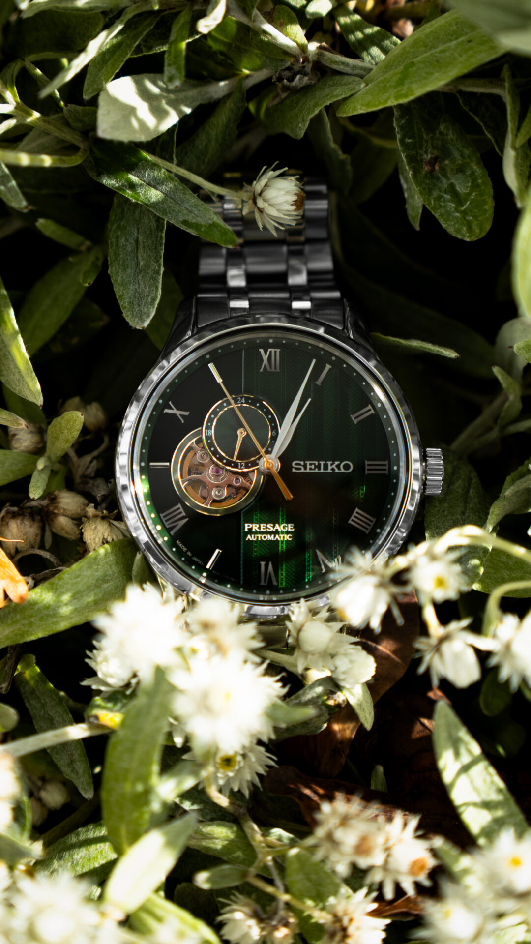 Silberne Uhr mit grünem Ziffernblatt in einem grünen Blumenbeet